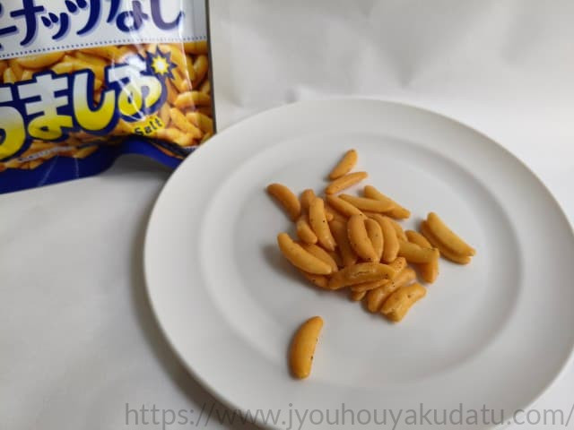 白い皿に盛られた「亀田の柿の種 うましお（ピーナッツなし）」。醤油味とは異なる、白っぽい色合いの柿の種が並んでいる。
