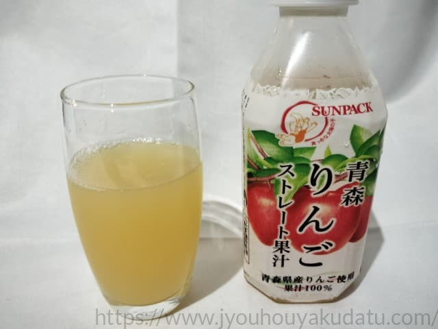 透明なグラスに注がれた、濃い黄色（琥珀色）のリンゴジュース。表面にわずかな泡が立ち、濃厚さが伝わってくる。