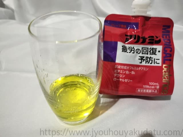 透明なグラスに注がれた、鮮やかな黄色のゼリー飲料。アリナミンメディカルバランスS グレープ風味の中身。