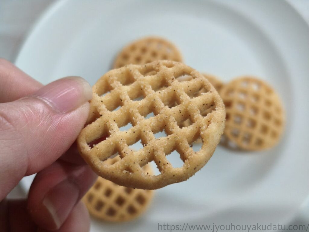 指でつまんだあみじゃが テキサスバーベキュー味と指についたパウダー