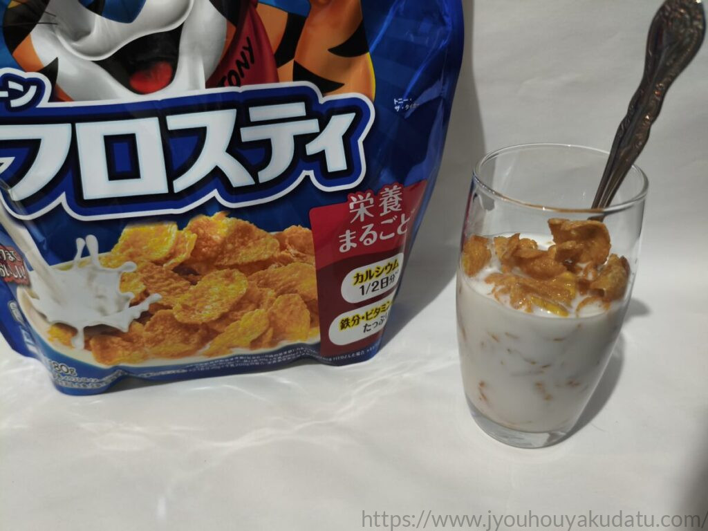 コーンフロスティに牛乳をかけてスプーンを入れた透明なグラス