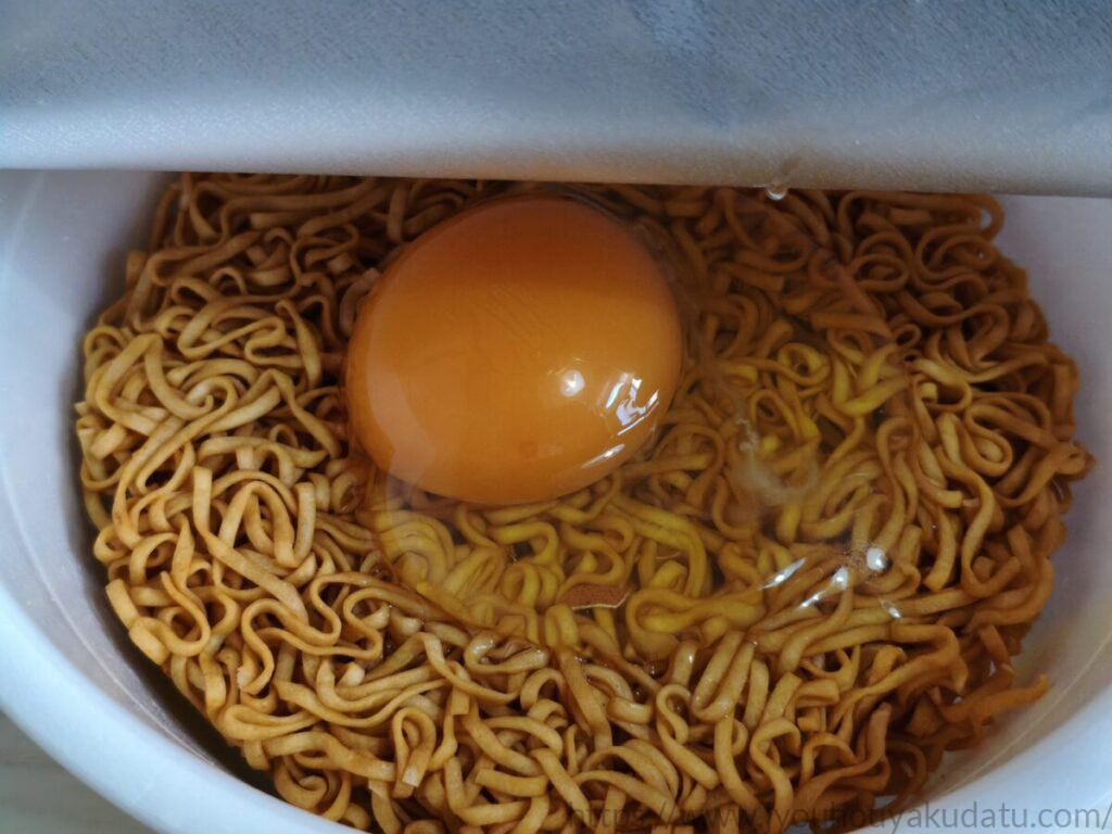 チキンラーメンどんぶりのたまごポケットに生卵を割り入れた状態。黄身が麺の中央に収まっている